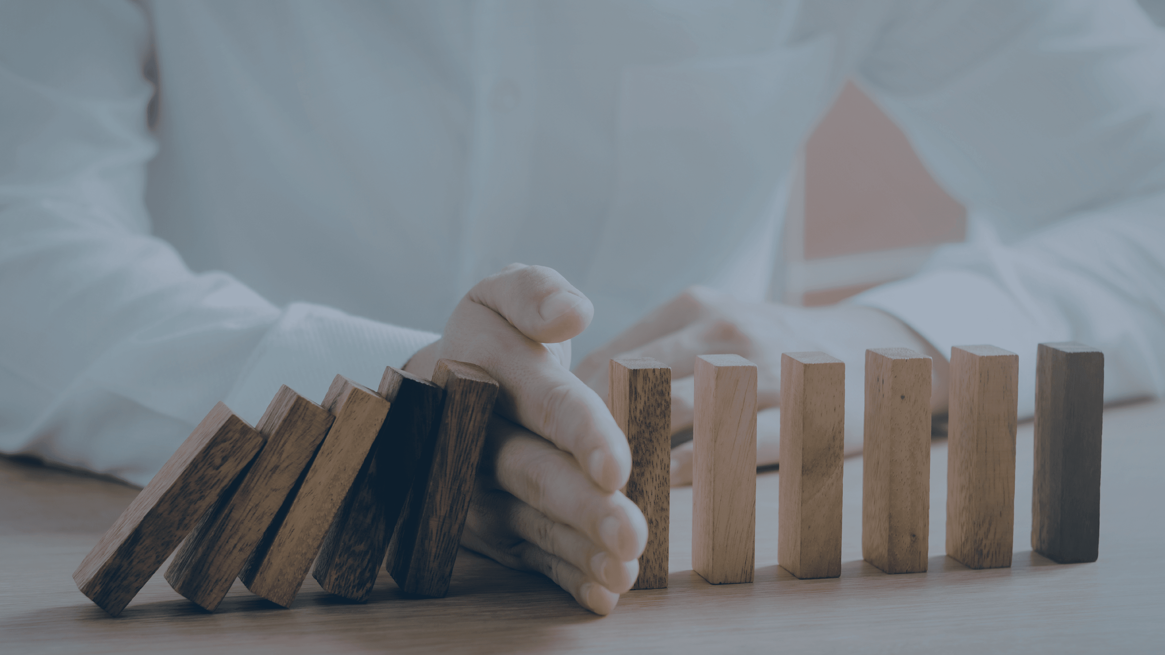 Hånd stopper væltende dominobrikker og illustrerer risikostyring, kontrol og forebyggelse af økonomiske fejl.